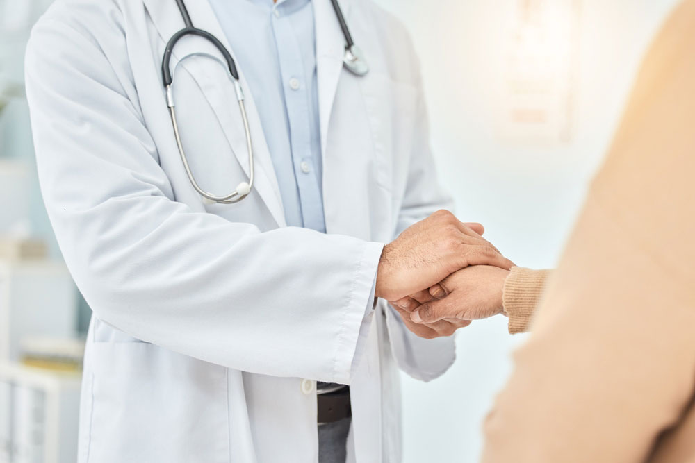 Close up of doctor wearing a lab coat and stethoscope holding a patient's hand