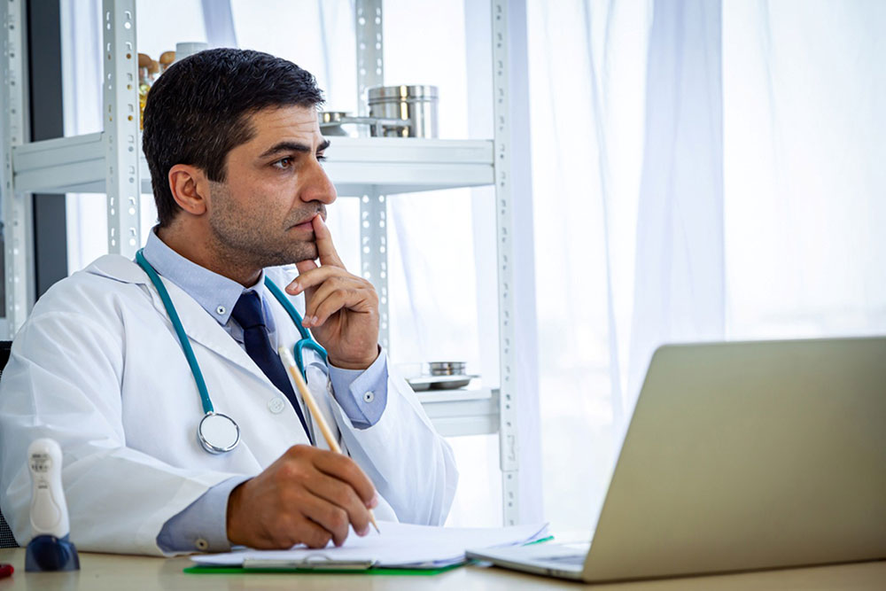 Doctor at desk with hand on chin looking thoughtful