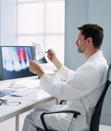 Dentist sitting at desk comparing dental imaging to X Ray film